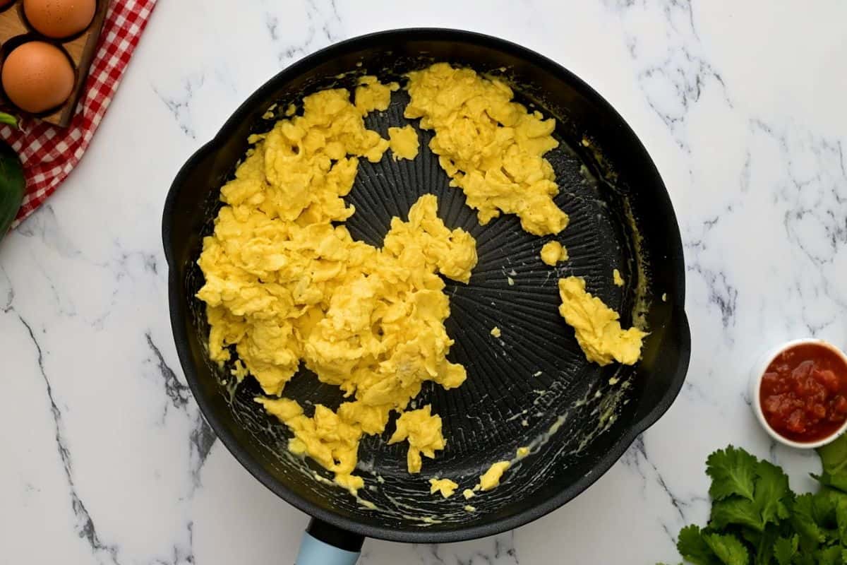 Fluffy scrambled eggs in skillet next to cilantro and salsa.