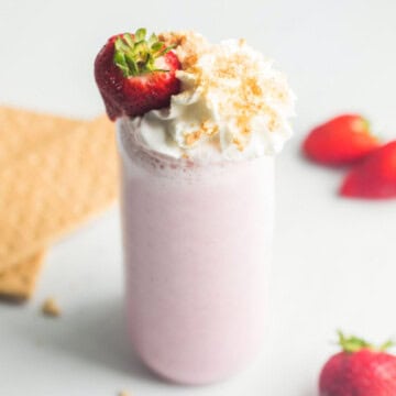 Strawberry Smoothie made with cottage cheese topped with whipped cream with crushed graham crackers on top and fresh strawberries in background.