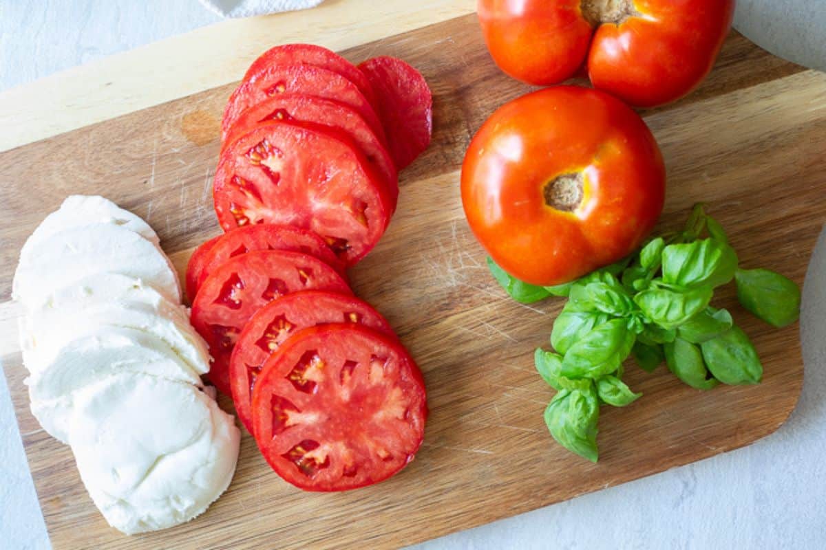 Fresh mozzarella, fresh tomatoes and basil on wooden cutting board.