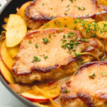 Close up of pork chops with apples in saute pan topped with fresh thyme leaves.