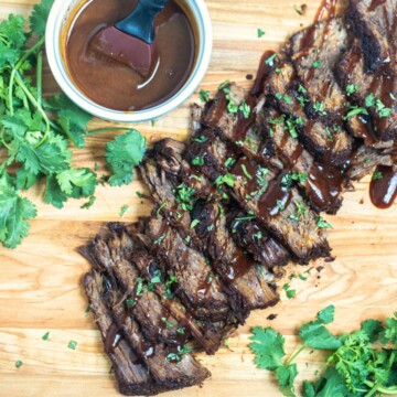 Sliced Instant Pot Brisket on wooden cutting board drizzled with BBQ sauce and parsley on the side.