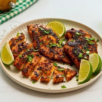 Blackened Chicken Breasts on plate with cilantro and lime wedges.