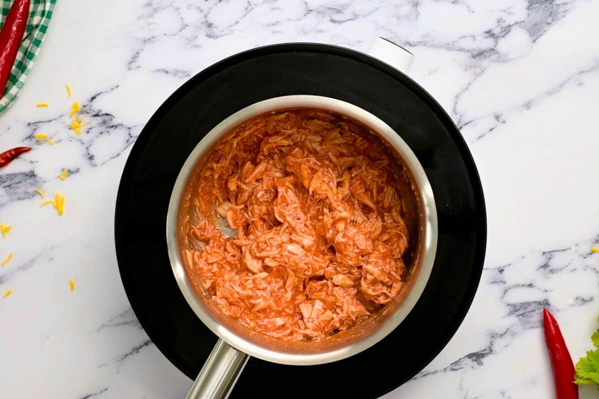 Shredded cooked chicken tossed with homemade buffalo sauce in saucepan before adding to pizza.