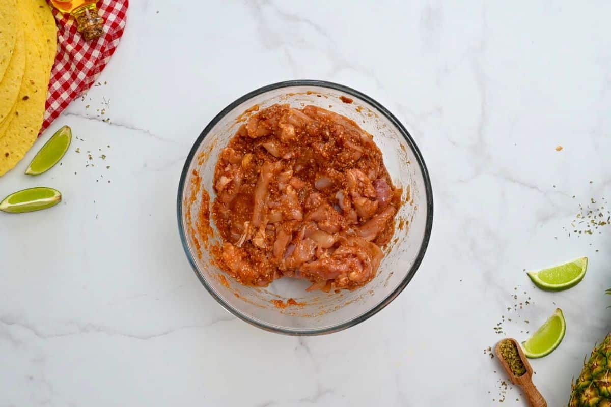 Sliced chicken thighs in mixing bowl tossed with al pastor marinade.