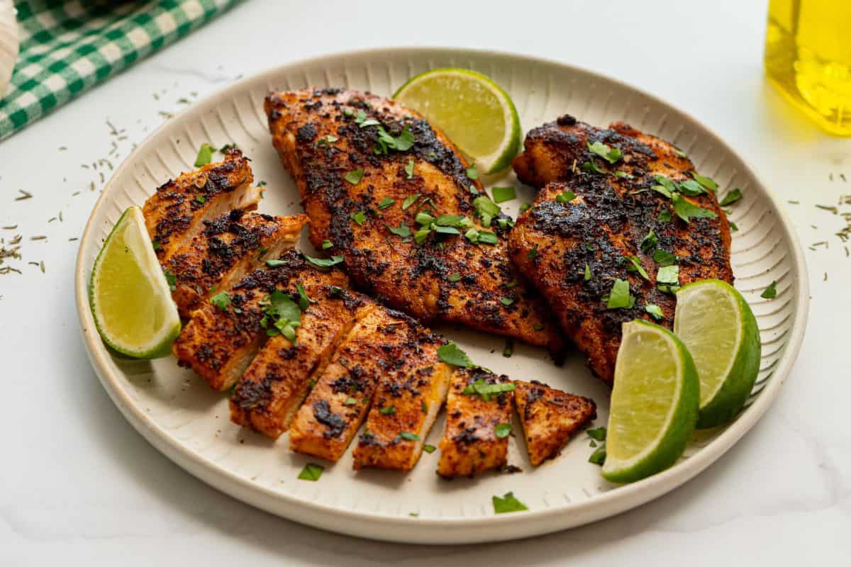 Blackened Chicken Breast on plate with minced cilantro and wedges of limes.