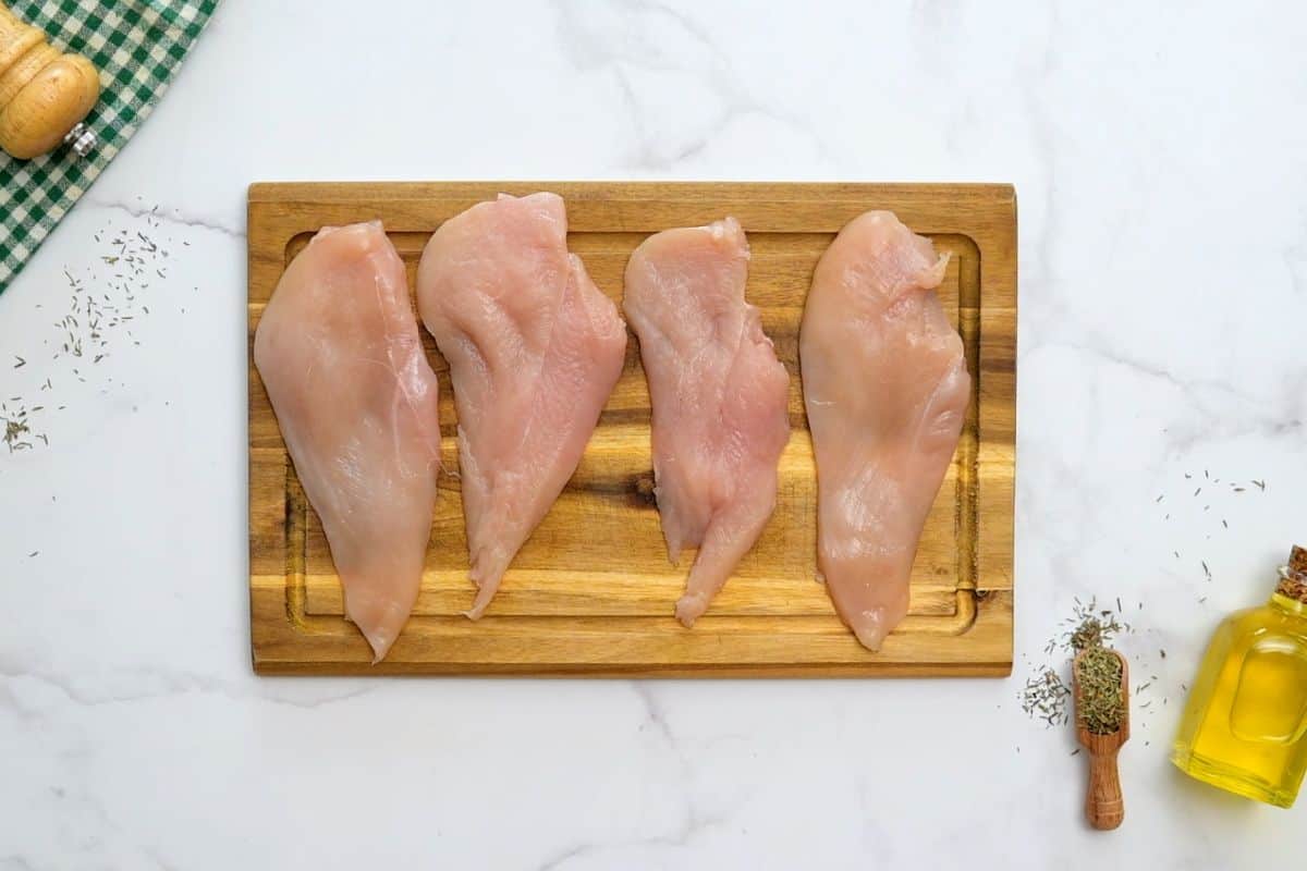 Chicken breasts cut into cutlets on wooden cutting board next to fresh thyme.