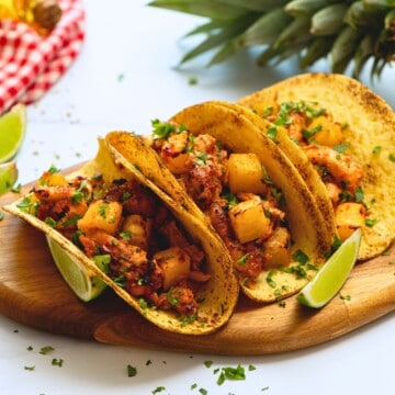 Chicken al pastor tacos on wooden tray with fresh lime wedges and minced cilantro.