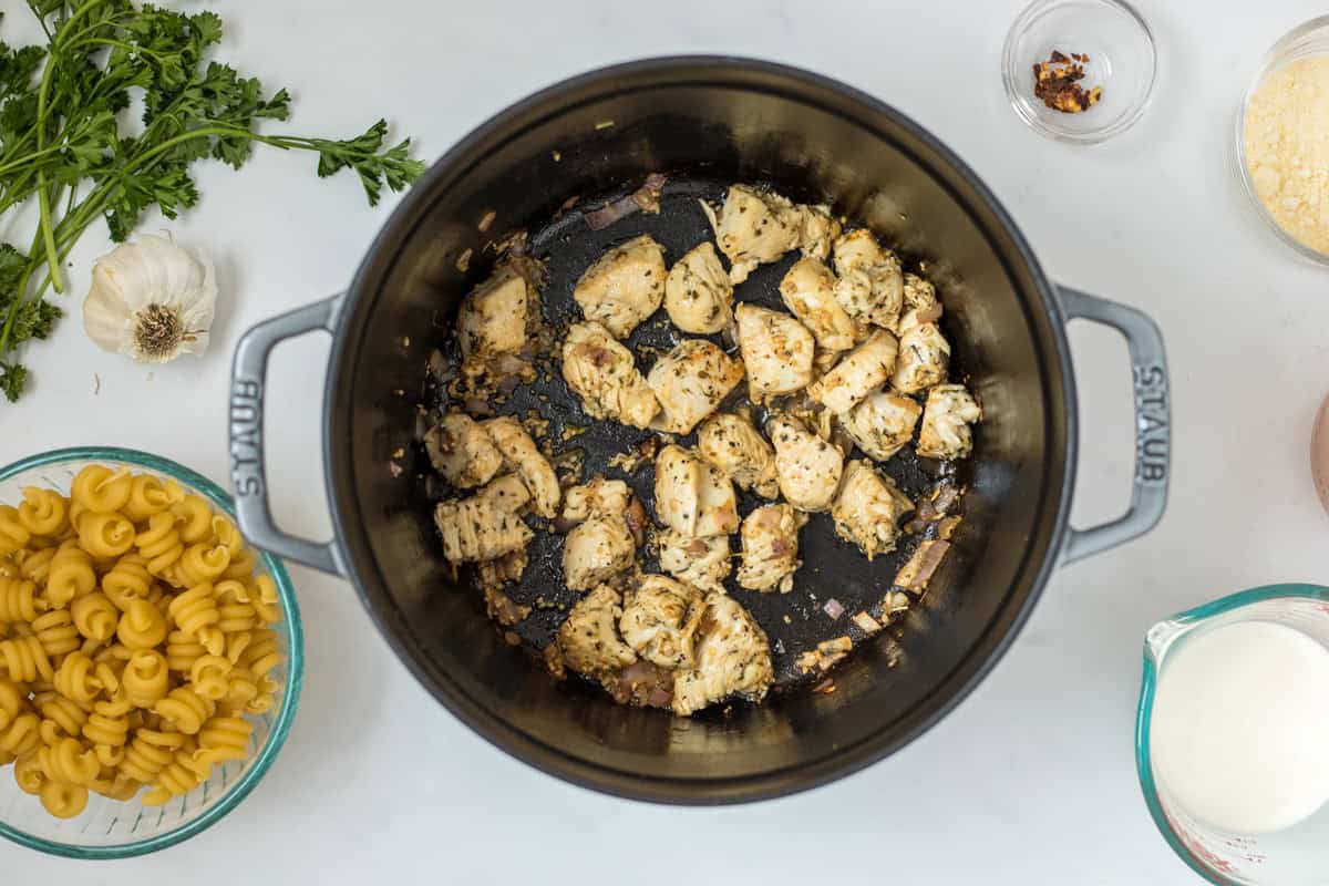 Seared boneless skinless chicken breast chunks tossed in Italian seasoning in dutch oven with pasta and cream to the side.