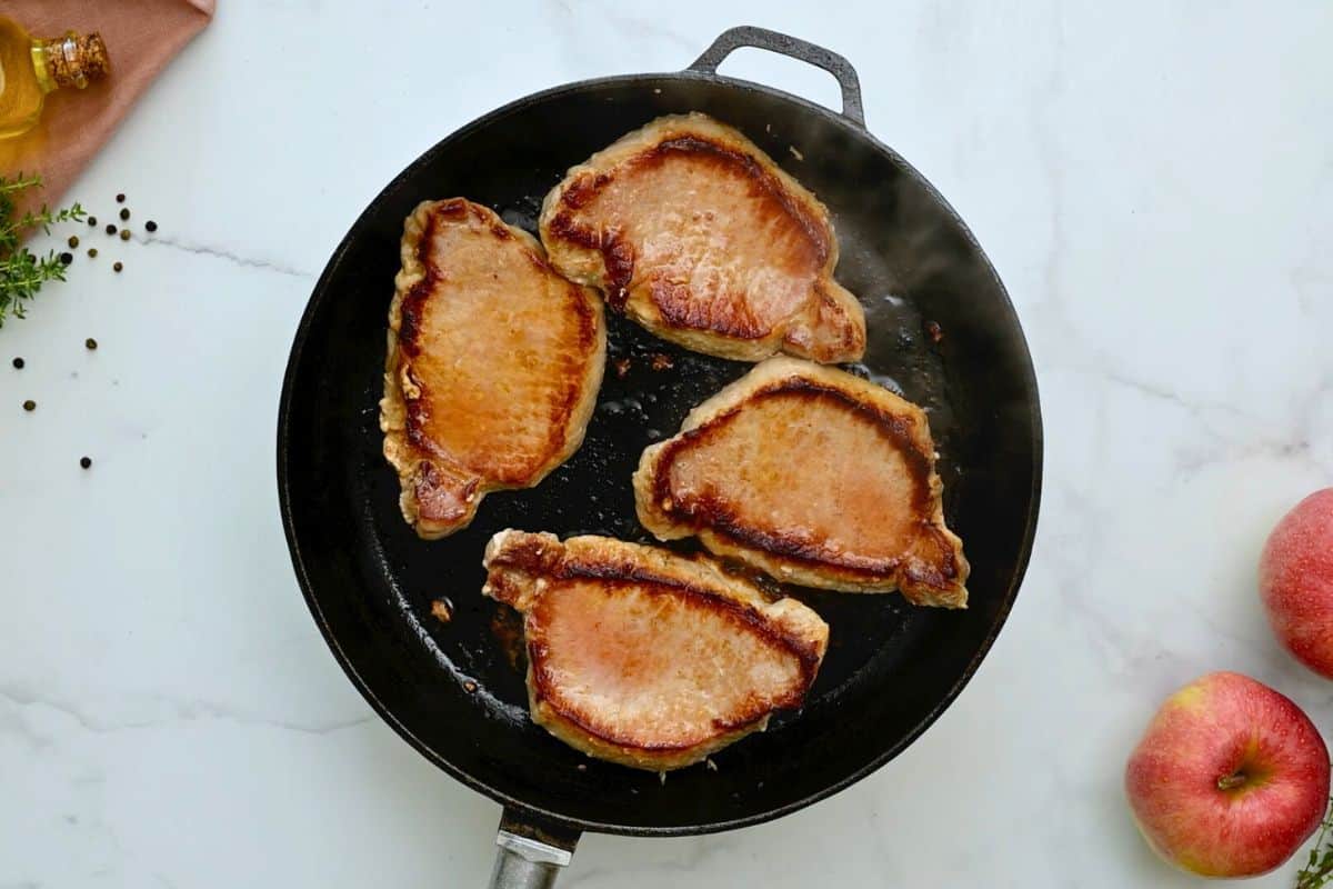 Four boneless pork loin chops in skillet after being seared.