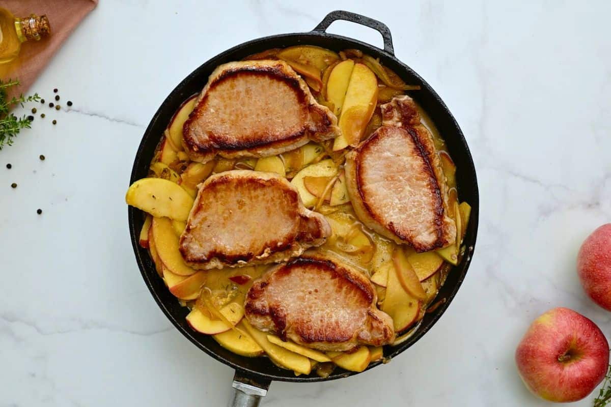 Seared pork chops nestled in apples and onions in skillet.