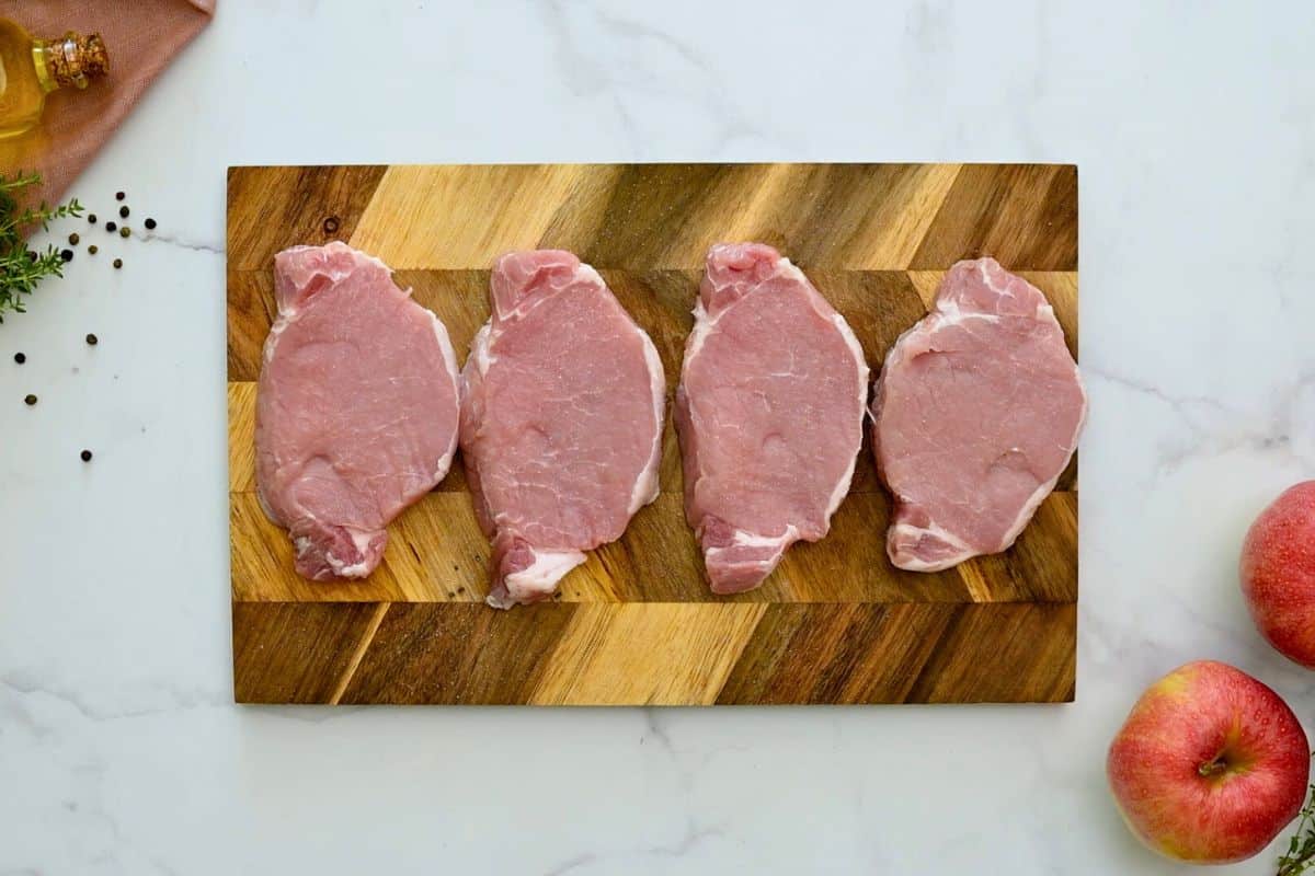 Four boneless pork chops on wooden cutting board seasoned heavily with salt.