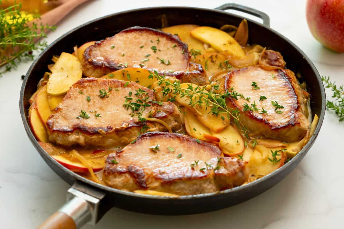 Pan seared pork chops in skillet with sauteed apples and onions.