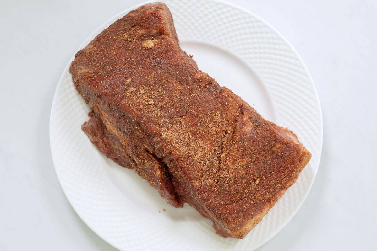 Beef brisket on white plate covered with sweet and savory spice rub.