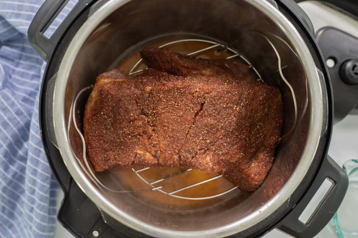 Spice rubbed brisket on metal trivet over apple juice inside Instant Pot.