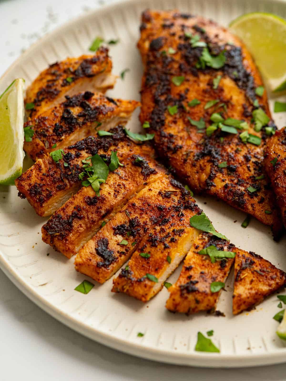 Blackened Chicken Breasts on plate with cilantro and lime wedges.