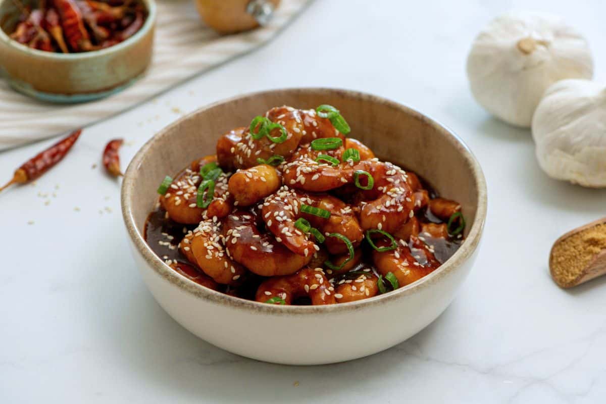 Bowl of sauteed shrimp with general tso sauce topped with sesame seeds and green onions.