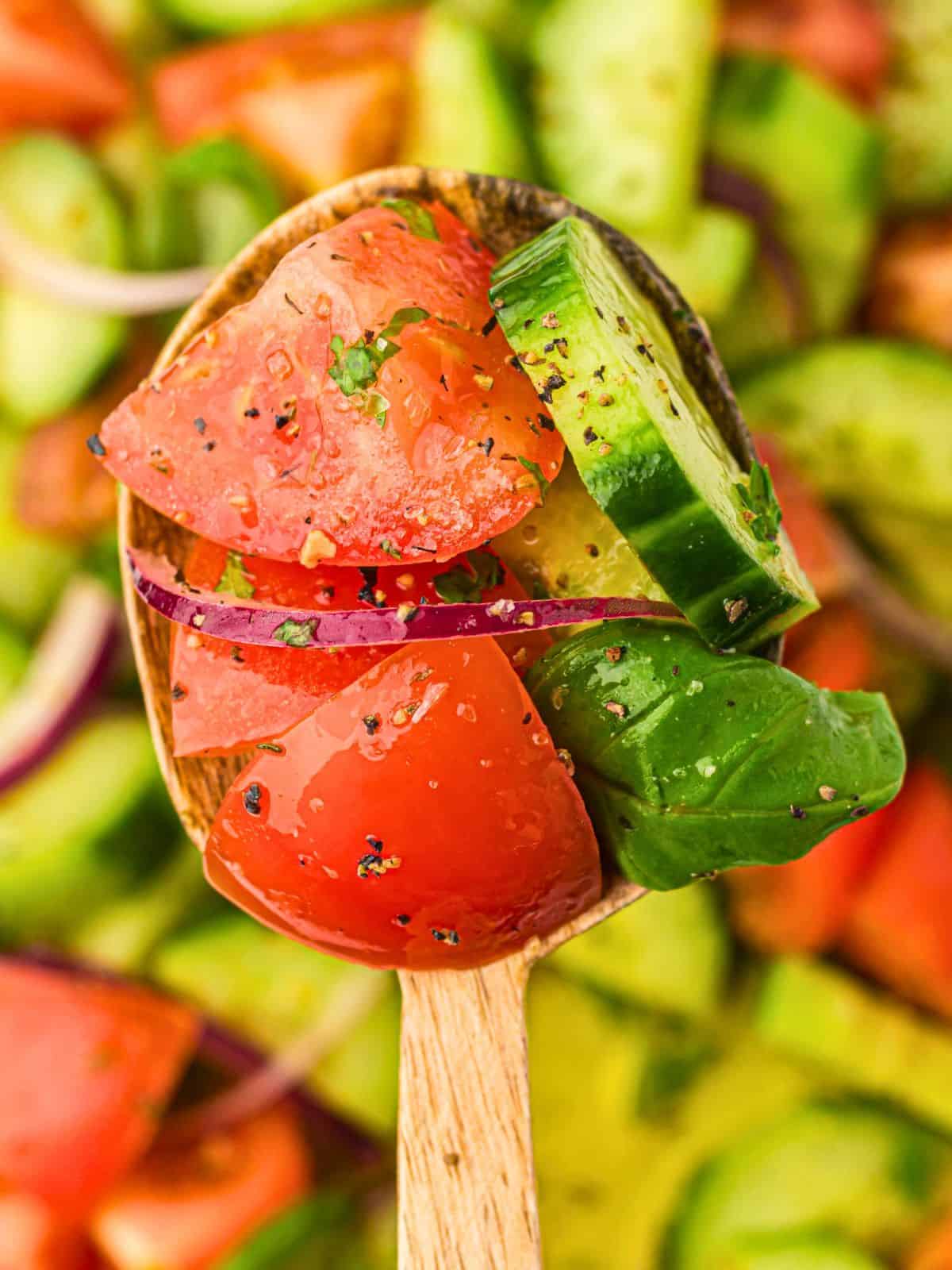 Tomato and cucumber salad being scooped out of large bowl with wooden spoon.