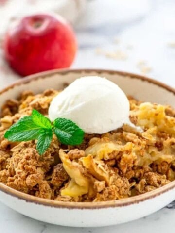 Bowl of Apple Crisp Recipe with oats served in bowl topped with ice cream and mint.