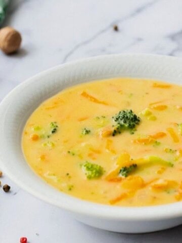 Bowl of Broccoli Cheddar soup in white bowl with nutmeg in background.