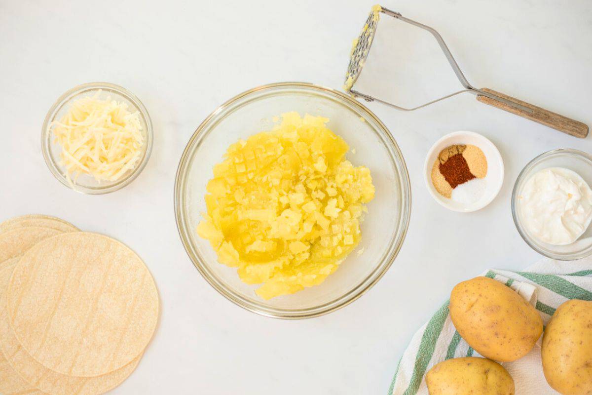 Cooked Yukon Gold potatoes in mixing bowl next to sour cream and seasonings on side.