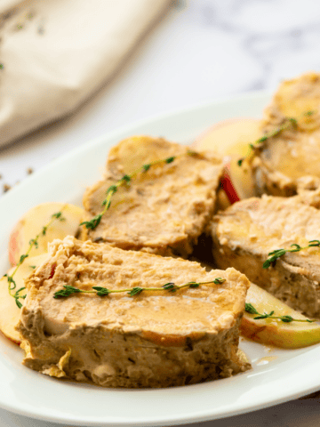 Sliced slow cooker pork roast on platter with thyme leaves.