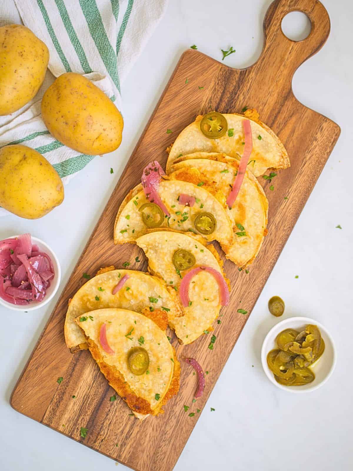 Crispy potato tacos on wooden cutting board topped with pickled red onions and pickled jalapenos.