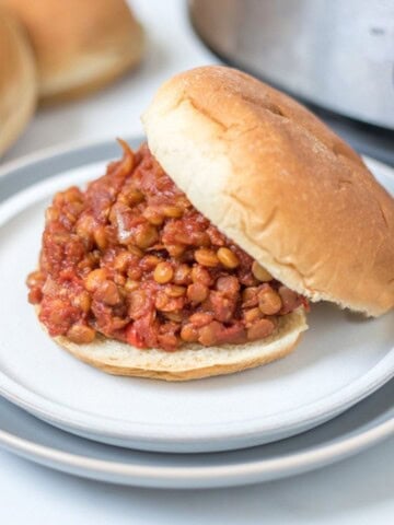 Vegan Sloppy Joe made with lentils served on a bun on a plate with the crockpot in the background.