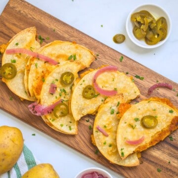 Crispy potato tacos on wooden cutting board topped with pickled red onions and pickled jalapenos.