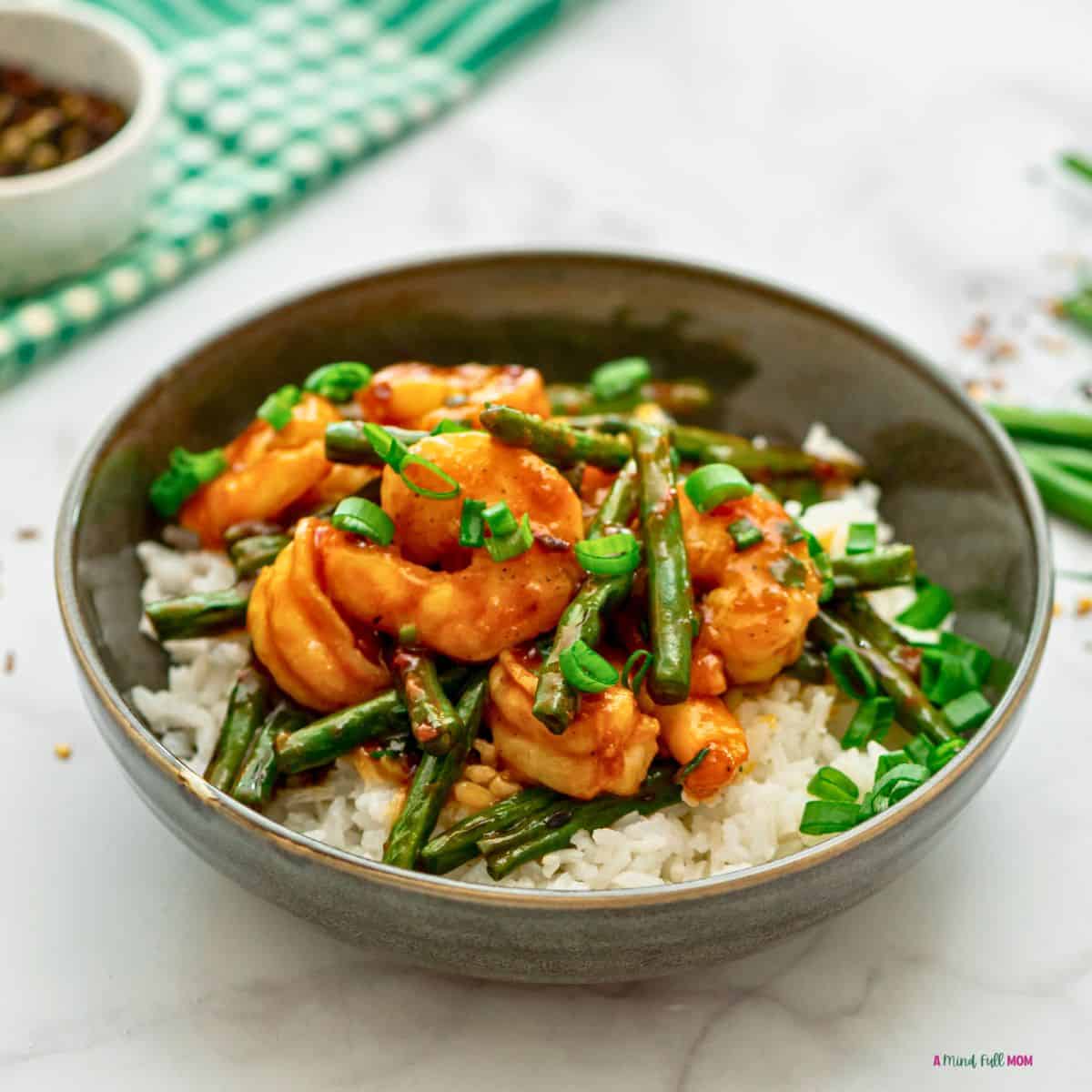 Bowl of stir fry shrimp with hunan sauce and green beans served over cie.