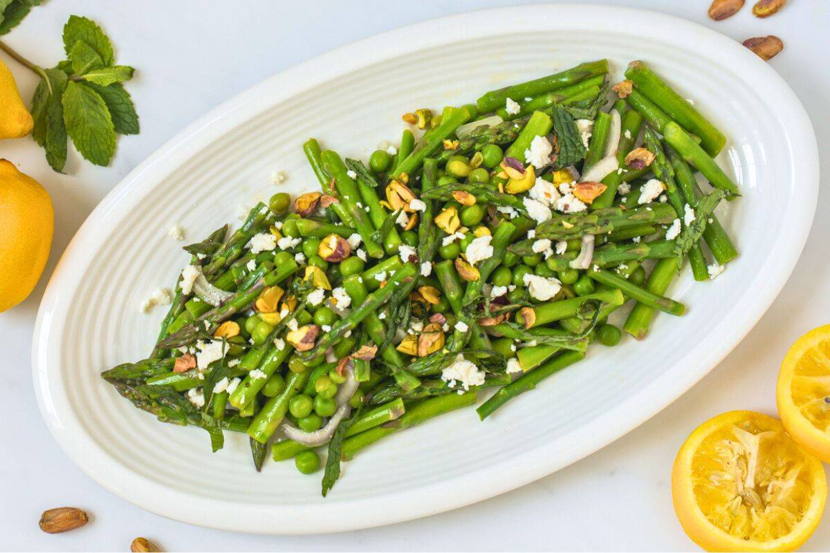 Easter Dinner Salads Asparagus and pea salad plated on white plate topped with crumbled feta, chopped pistachios, and mint.