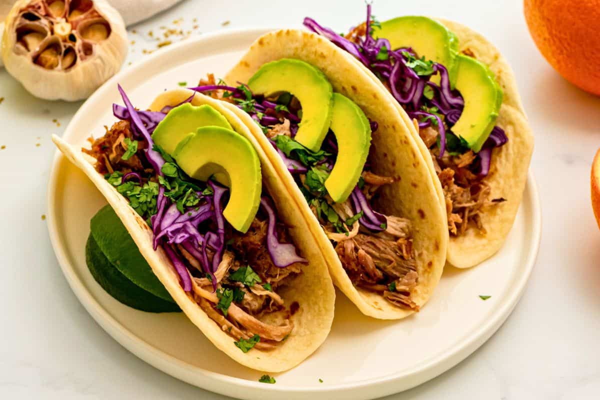 Simple cinco de mayo party menu Instant Pot carnita meat served on flour tortillas with cabbage and lime juice and avocado.