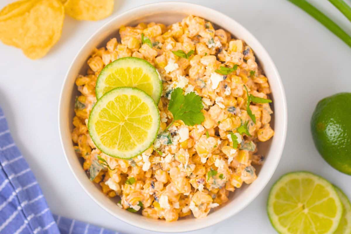 Cinco de Mayo Side Dishes Street Corn Salad with creamy lime dressing in white bowl topped with lime slices and cotija cheese.