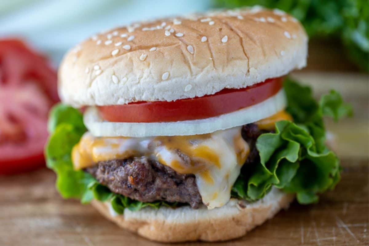 Homemade Burger on cutting board on bun topped with with lettuce and tomatoes.
