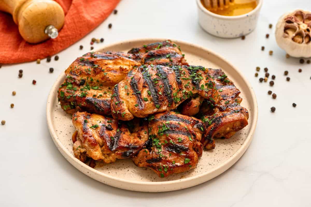 Grilled marinated chicken thighs on platter topped with minced parsley.