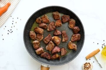 Browned chunks of floured chuck roast in skillet for base of beef stew.