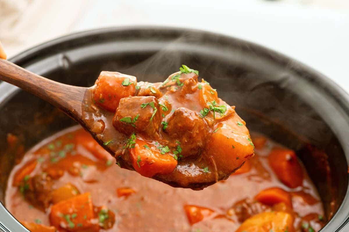 Spoonful of crockpot beef stew with potatoes, carrots, and chuck roast coming out of slow cooker.