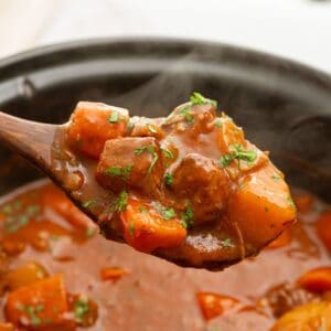 Spoonful of beef stew coming out of slow cooker with tender beef, carrots, and potatoes.