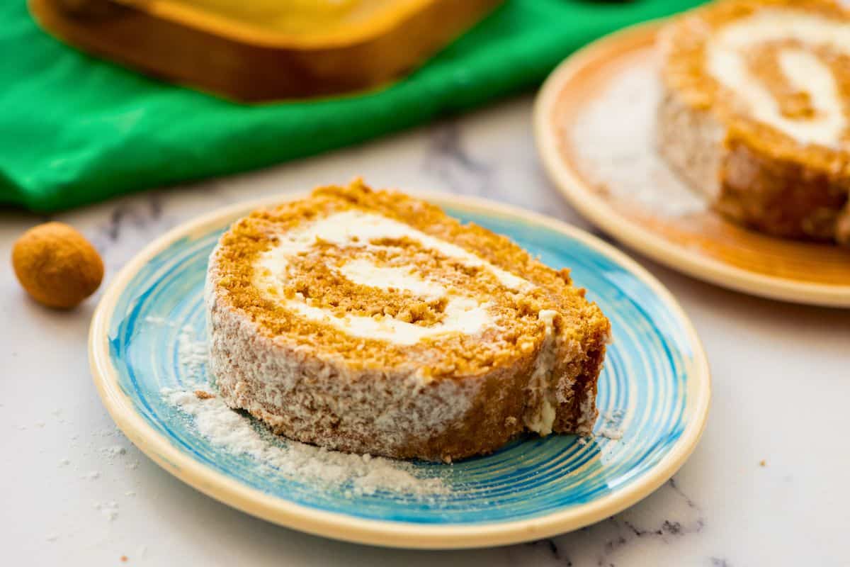 Desserts to Make-Ahead for Thanksgiving Sliced Pumpkin Roll with cream cheese filling on plates dusted with powdered sugar.