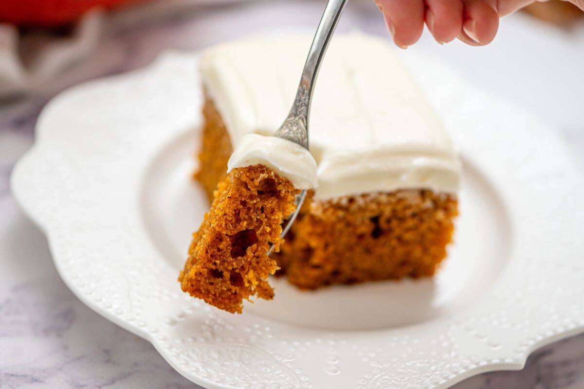 Desserts to Make Ahead for Thanksgiving Slice of fluffy pumpkin cake on white plate topped with cream cheese frosting with fork taking a bite.