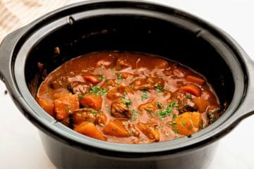Beef Stew thickened in crockpot topped with parsley.