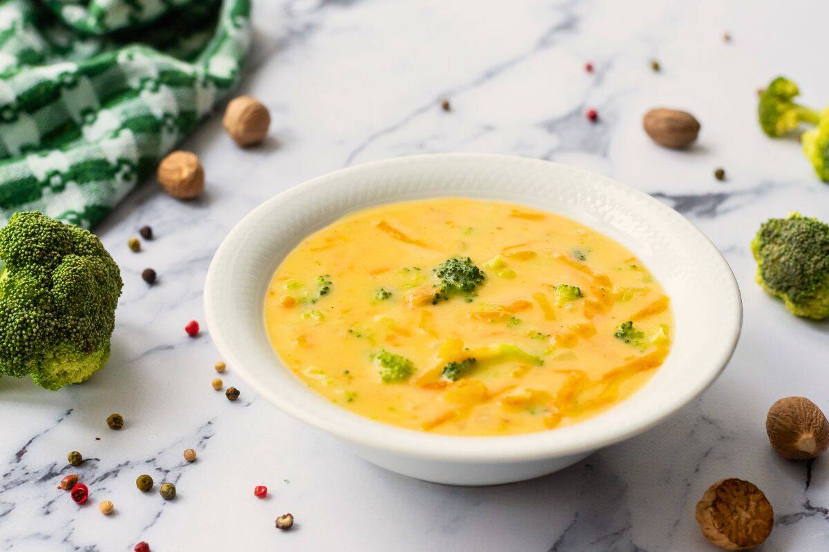 Favorite Soup Recipes Bowl of cheddar broccoli soup next to peppercorns and nutmeg.
