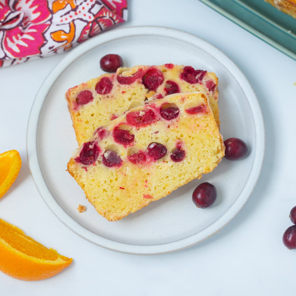Cranberry Orange Bread Two slices of cranberry orange bread on plate next to fresh cranberries and orange slices.