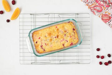 Baked cranberry orange quick bread in glass loaf pan on wire cooling rack.