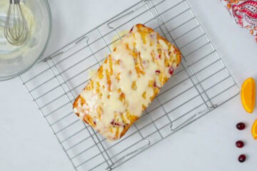 Cranberry Orange Loaf on wire cooling rack after being drizzled with simple orange glaze.