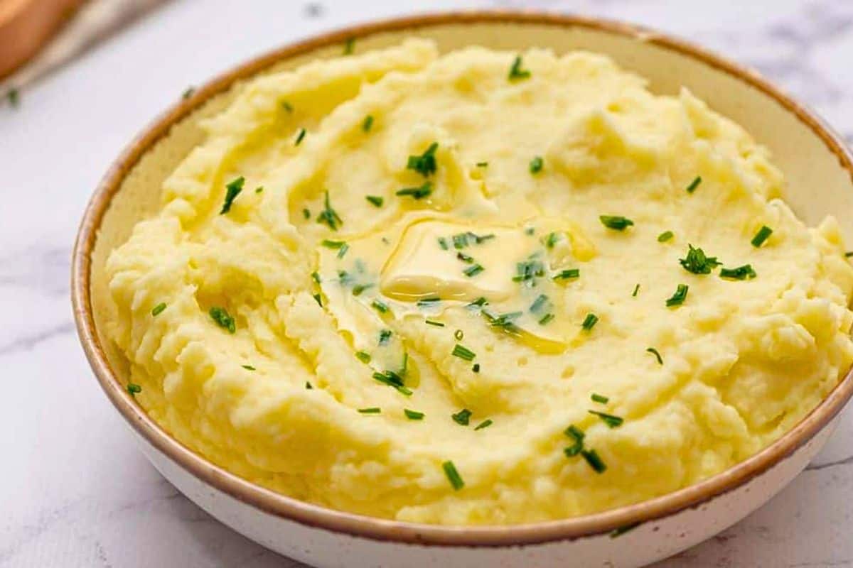 Thanksgiving Recipe to Make Ahead Bowl of creamy gold mashed potatoes topped with butter and chives.