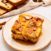 Slice of overnight breakfast casserole made with cinnamon raisin bread, eggs, cubed ham, sharp cheddar, and eggs on plate topped with maple syrup and powdered sugar.