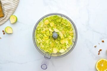 Food Processor with shaved brussels sprouts inside.