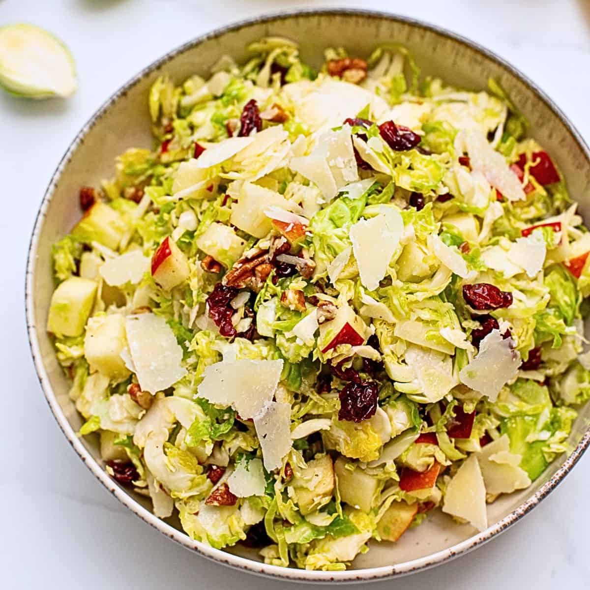Easy Ideas for Christmas Dinner Salad dished out made with shaved Brussels Sprouts tossed with honey lemon dressing, diced apples, dried cranberries, shaved parmesan, and chopped toasted pecans.