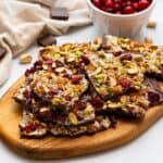 Chocolate bark on cutting board made with chopped nuts, dried cranberries, and sea salt.