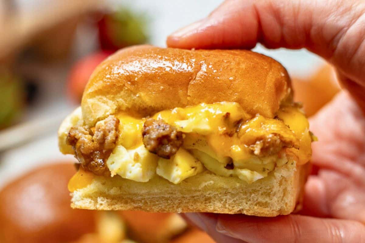Favorite Easter Brunch Recipes Hand holding breakfast slider made with Hawaiian roll, ausage, eggs, and cheese.